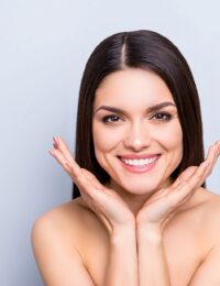 Portrait of gorgeous toothy woman presenting perfect smooth soft idyllic face skin isolated on grey background. Detox botox collagen vitamins minerals wellness wellbeing enhancement concept